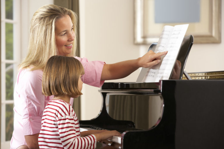 mother teaching her daughter how to read notes to play piano